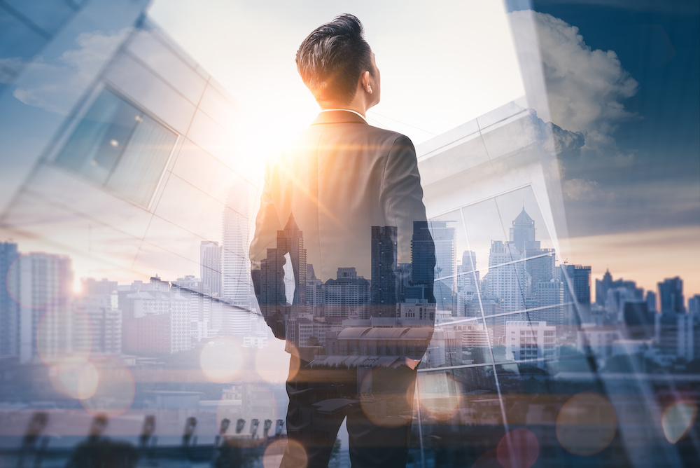 The double exposure image of the business man standing back during sunrise overlay with cityscape image. The concept of modern life, business, city life and internet of things.